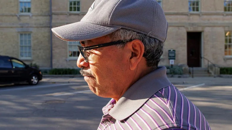 A man with glasses and a hat walks on the street.